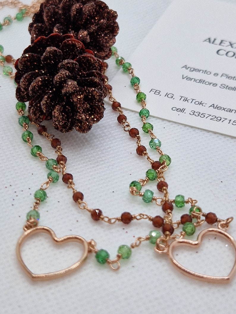 Collana artigianale con due fili di perle verdi e marroni, due ciondoli a cuore e decorazioni a forma di pigne glitterate.