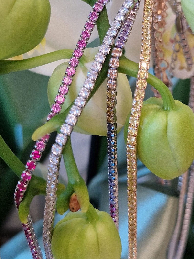 Una pila di bracciali con pietre preziose, in rosa, bianco e giallo, appoggiati su un'orchidea bianca.