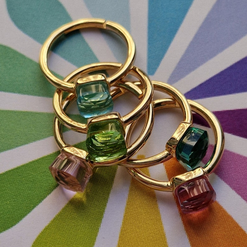 Anello portachiavi d'oro con sei piccoli ciondoli di cristallo sfaccettati e colorati su sfondo arcobaleno.