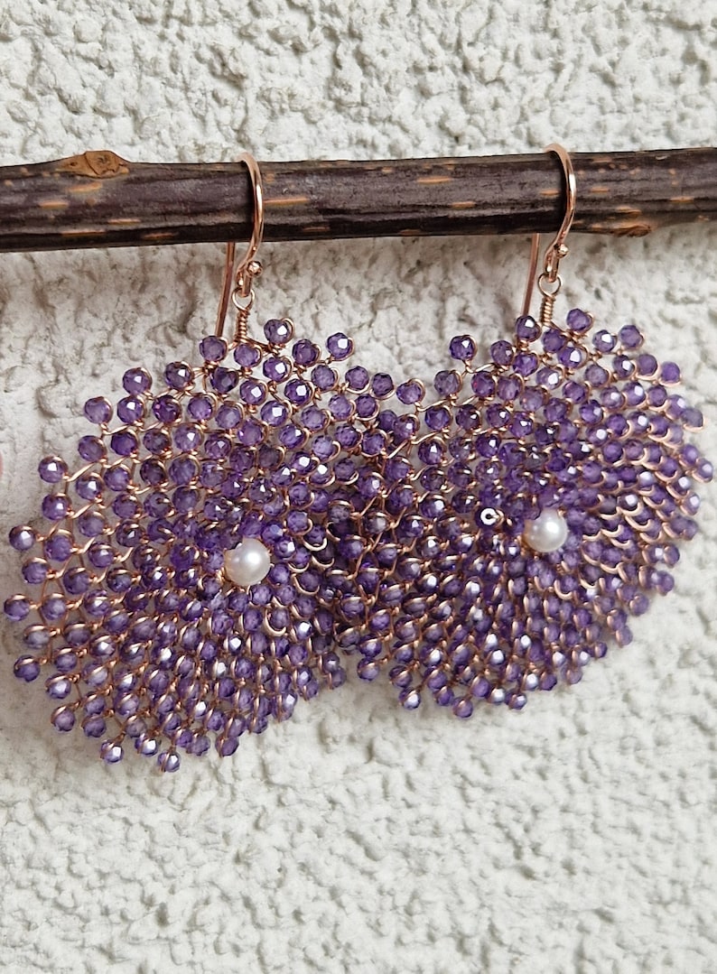 Orecchini a forma di fiore con perline di ametista e perla al centro, appesi a un ramo.