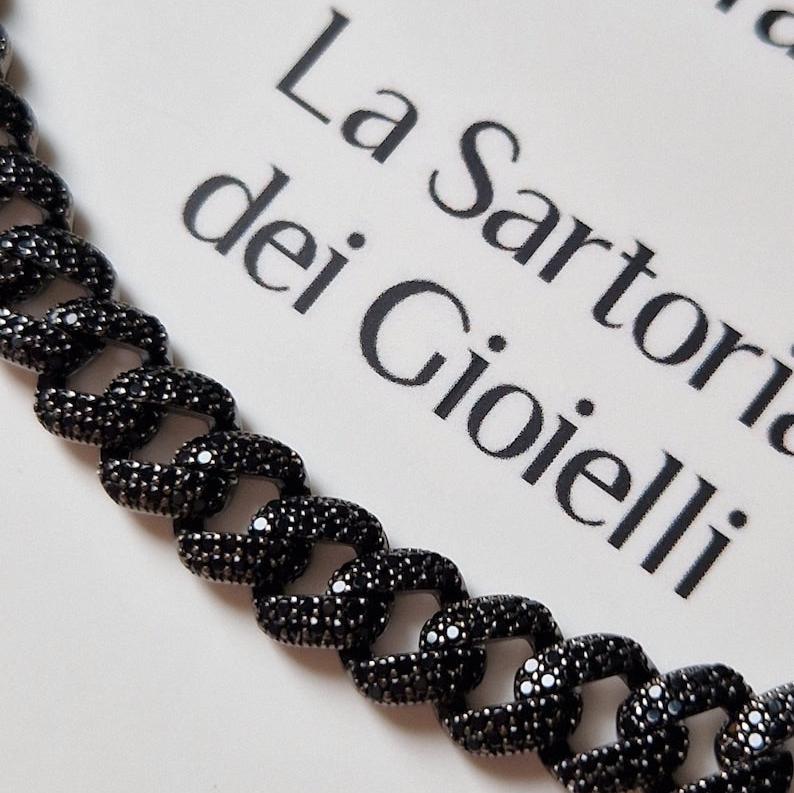 Collana a maglie cubane nera con pietre di zirconi scintillanti su uno sfondo con la scritta "La Sartoria dei Gioielli".