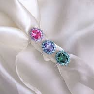 Tre anelli con pietre preziose rosa, viola e verde, su una sciarpa di seta.