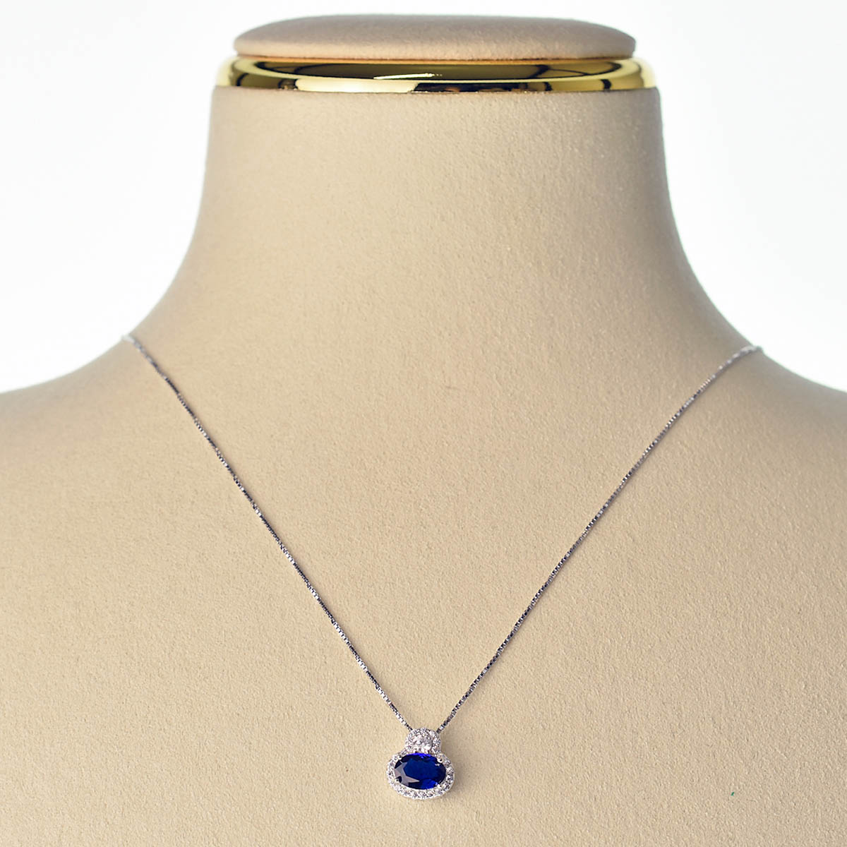 Collana in oro bianco con catena sottile e ciondolo con zaffiro ovale circondato da diamanti, esposta su manichino.