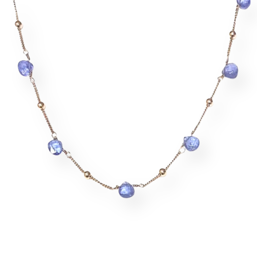 Collana d'oro con pietre tanzanite e perline dorate su sfondo bianco.
