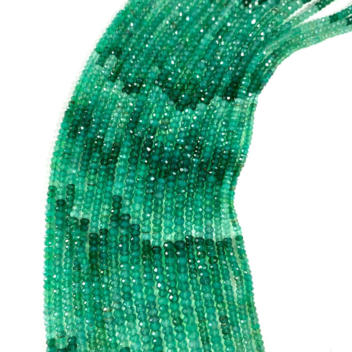 Fili di onice verde sfaccettati e cangianti su sfondo bianco.