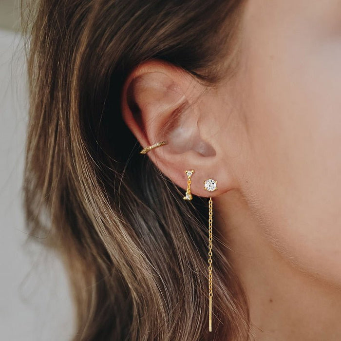 Un primo piano dell'orecchio di una donna con un set di orecchini d'oro.