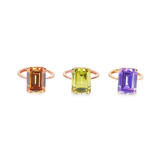 Tre anelli in oro rosa con pietre rettangolari: una arancione, una verde lime e una viola.