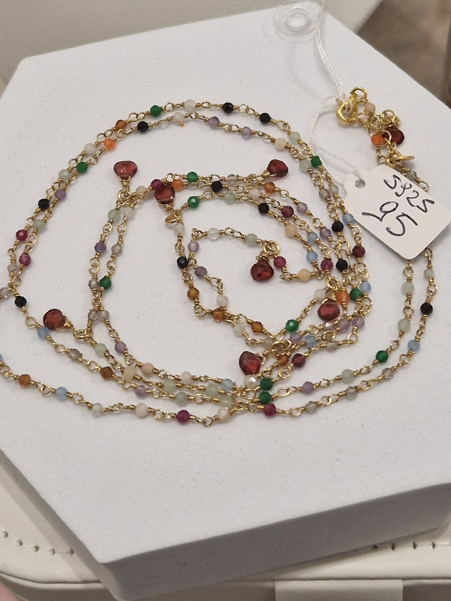 Collana in oro con pietre semipreziose e perle, avvolta su una scatola bianca, con cartellino del prezzo.