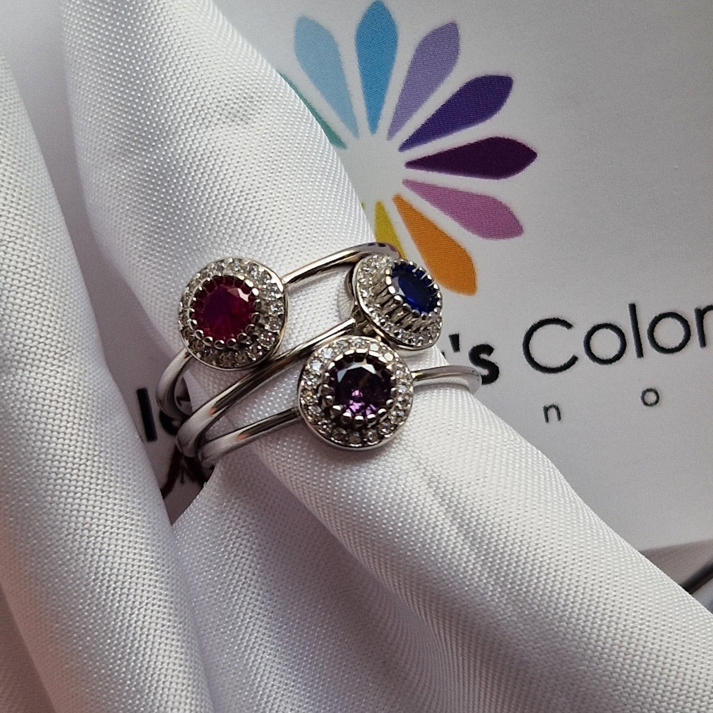Anello in argento con tre pietre preziose, rubino, zaffiro e ametista, circondate da piccoli diamanti.