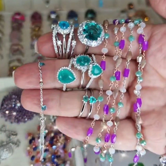 Una mano che mostra anelli e braccialetti in argento con pietre preziose azzurre e viola.