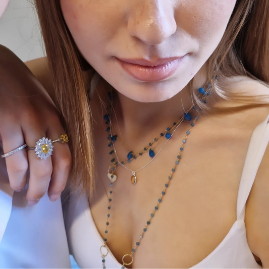 Donna che indossa anelli e collane d'oro con pietre preziose blu e gialle.