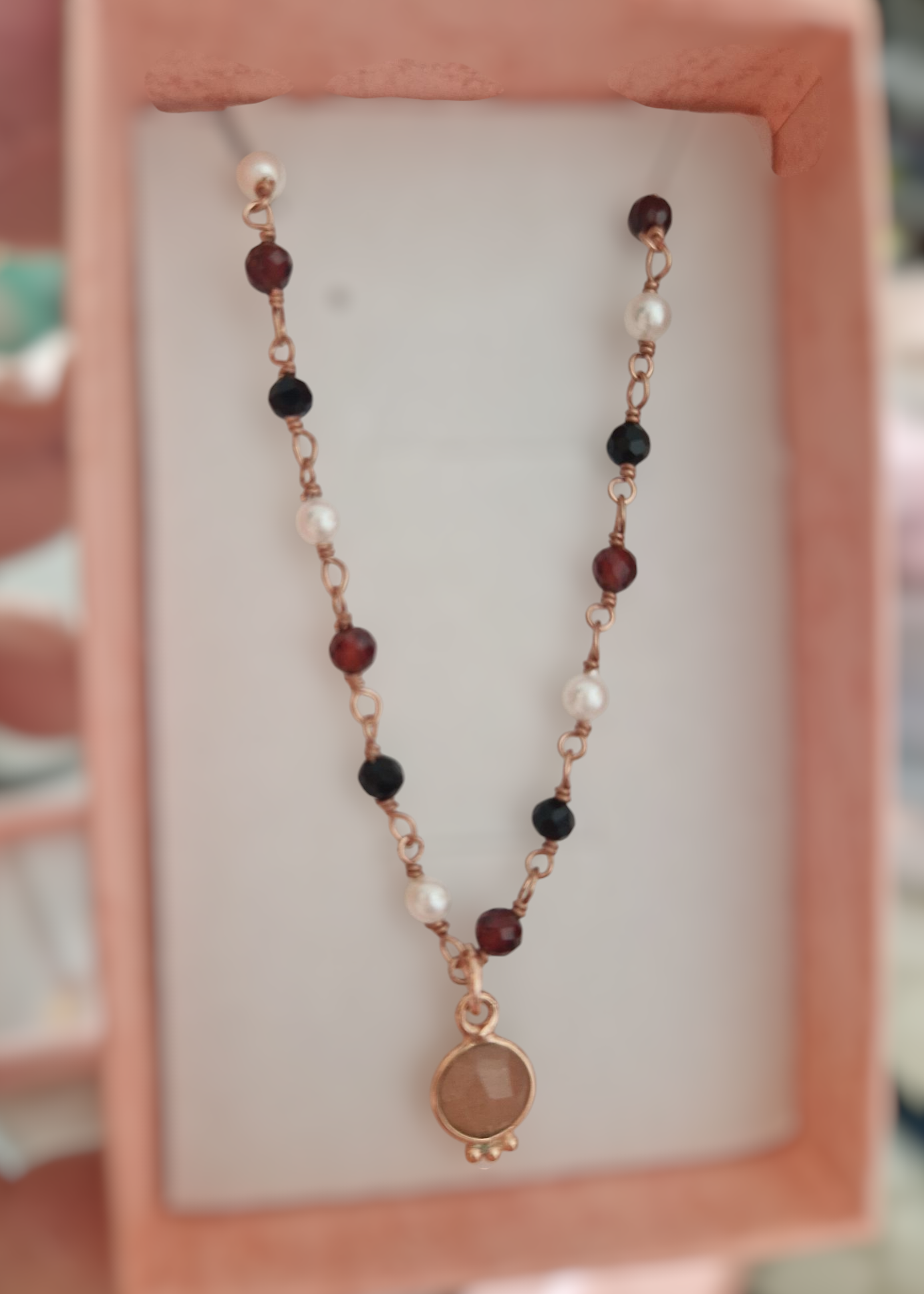 Collana fatta a mano con perle bianche, nere e rosse, con un ciondolo rotondo color ambra, in una scatola rosa.
