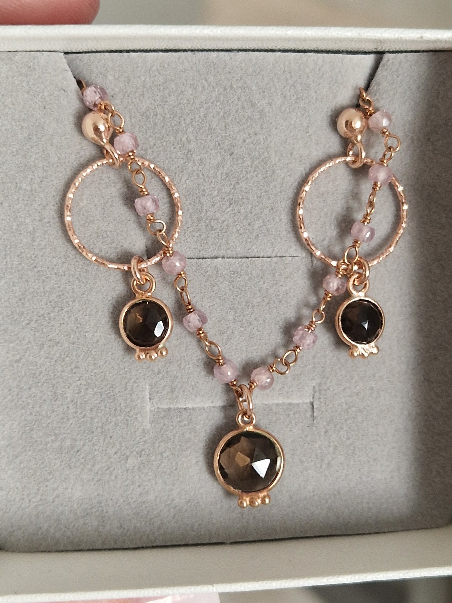 Collana in oro rosa con cerchi texturizzati, perle rosa e pietre scure, disposte su tre pendenti.