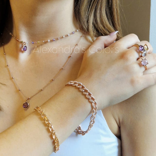 Giovane donna indossa gioielli in oro rosa con gemme viola: una collana, due braccialetti e anelli.