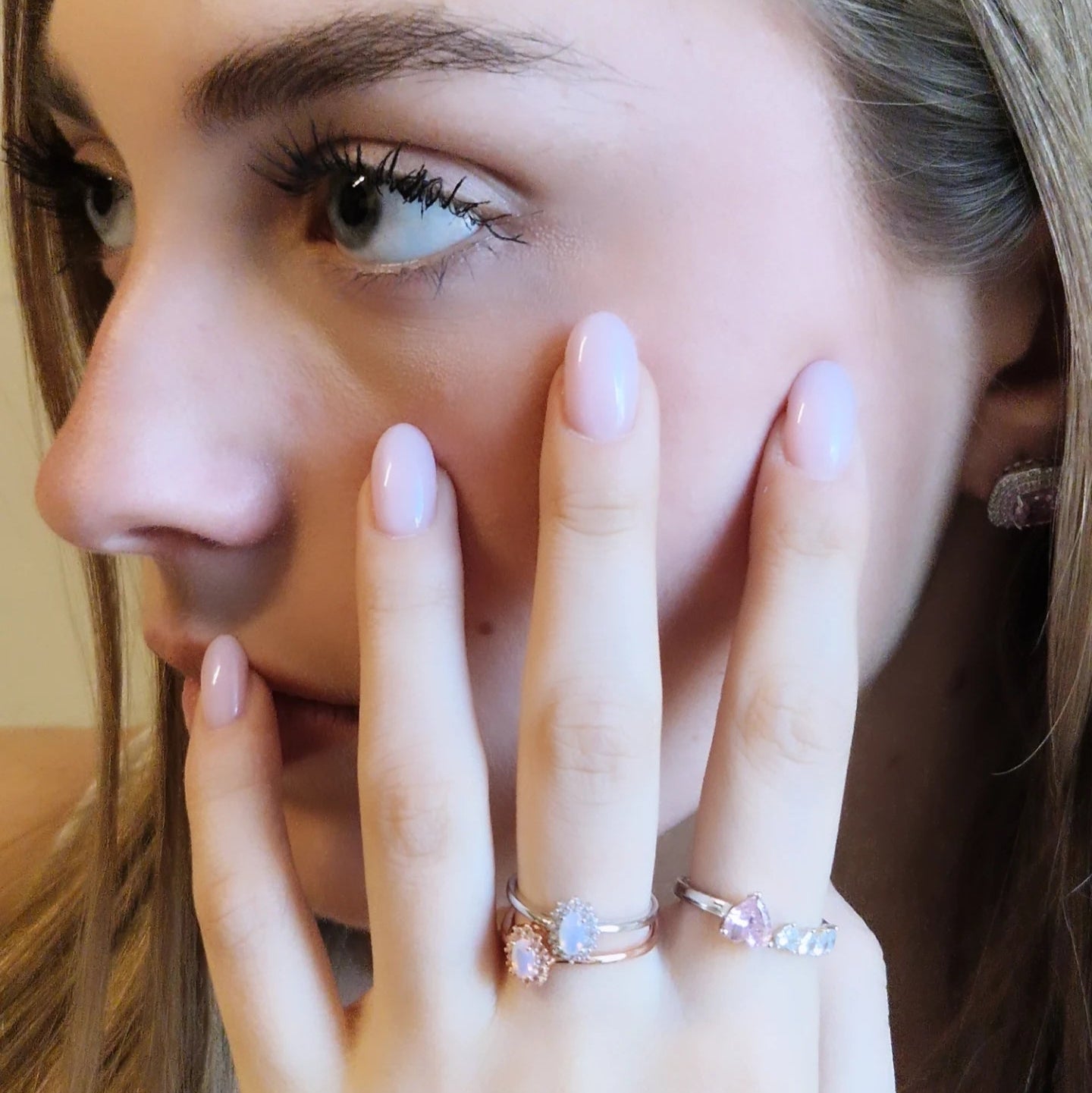 Giovane donna bionda con trucco leggero, manicure rosa chiaro e anelli con pietre preziose.