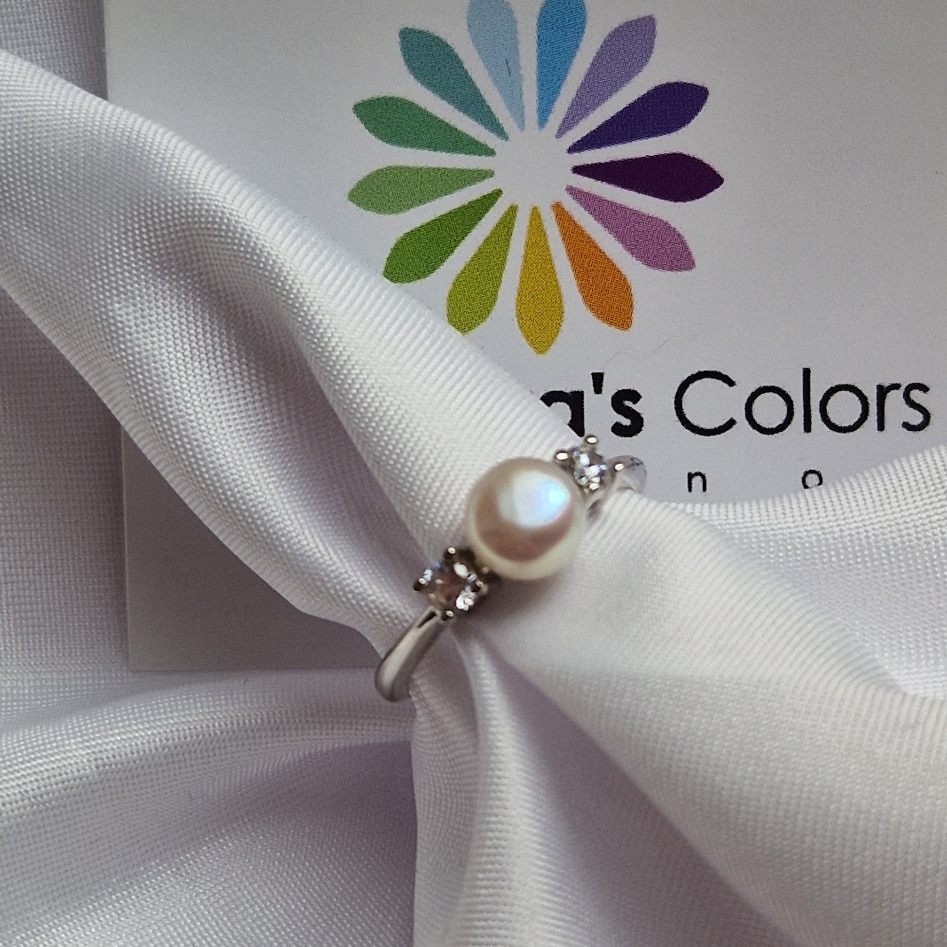 Anello in argento con perla bianca centrale e due zirconi su un panno di raso bianco.