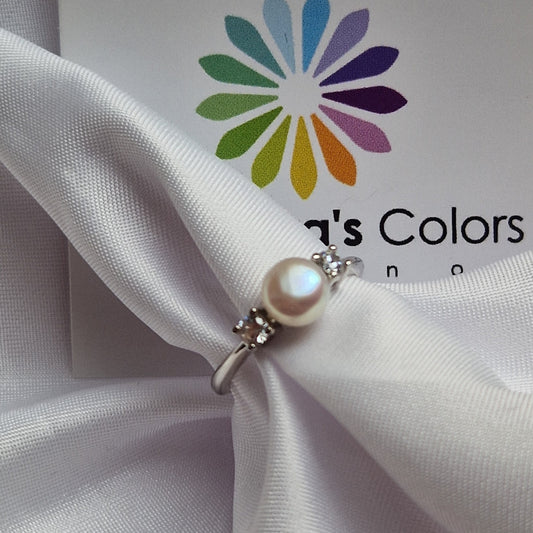 Anello in argento con perla bianca centrale e due zirconi su un panno di raso bianco.