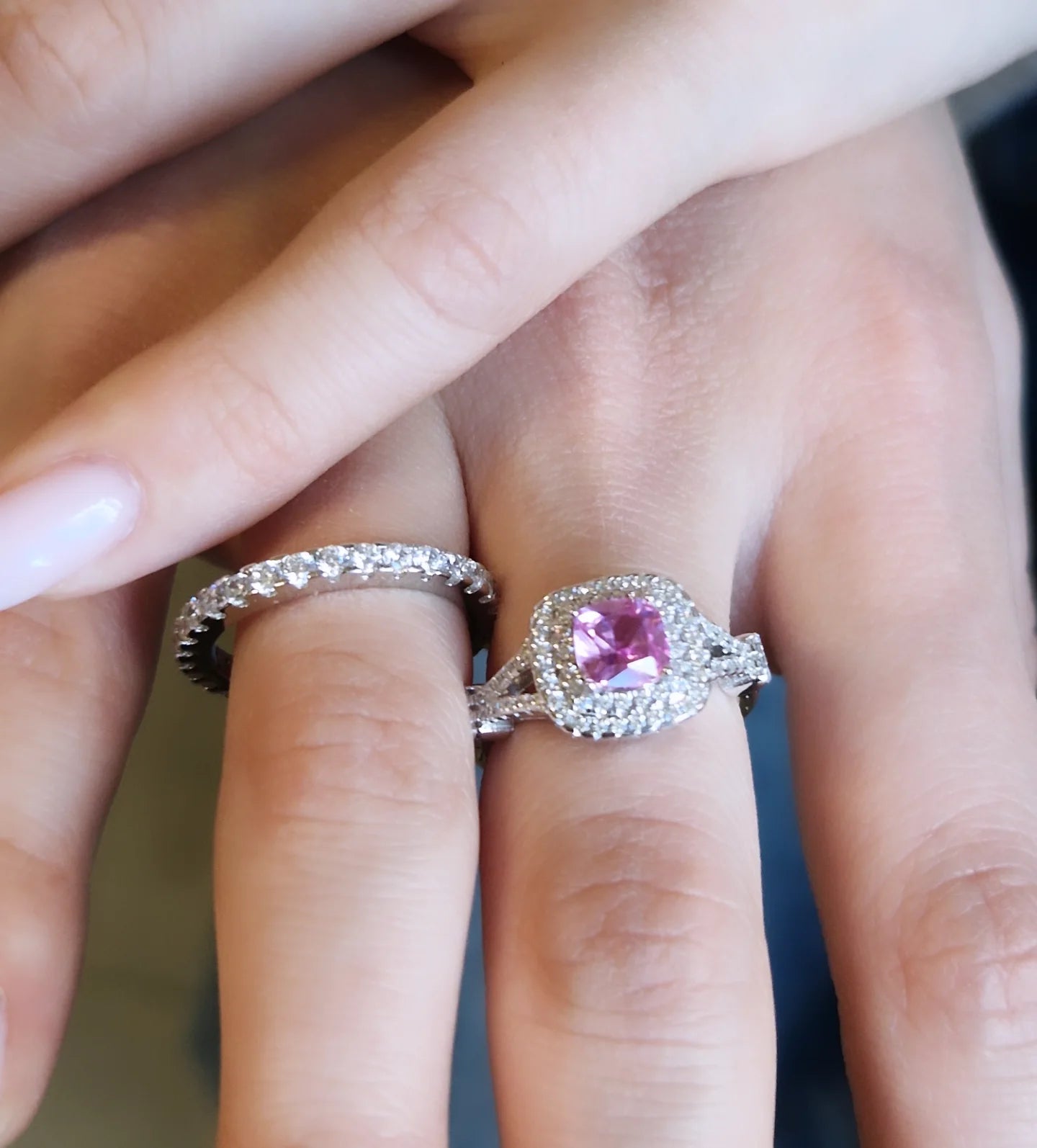Mano con anello di fidanzamento con diamante rosa taglio cuscino e fede nuziale con pavé di diamanti.