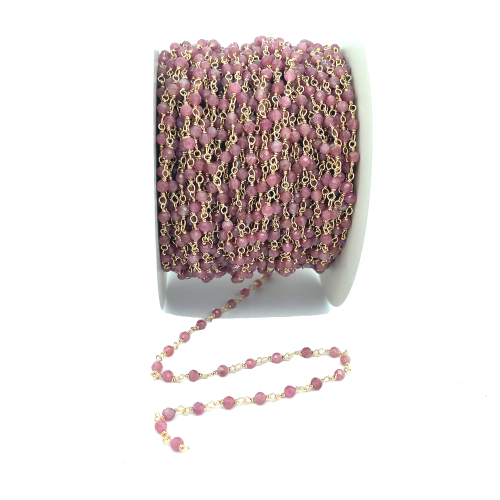 Catena a rosario con perle di tormalina rosa e finitura dorata su bobina bianca, con un tratto srotolato.