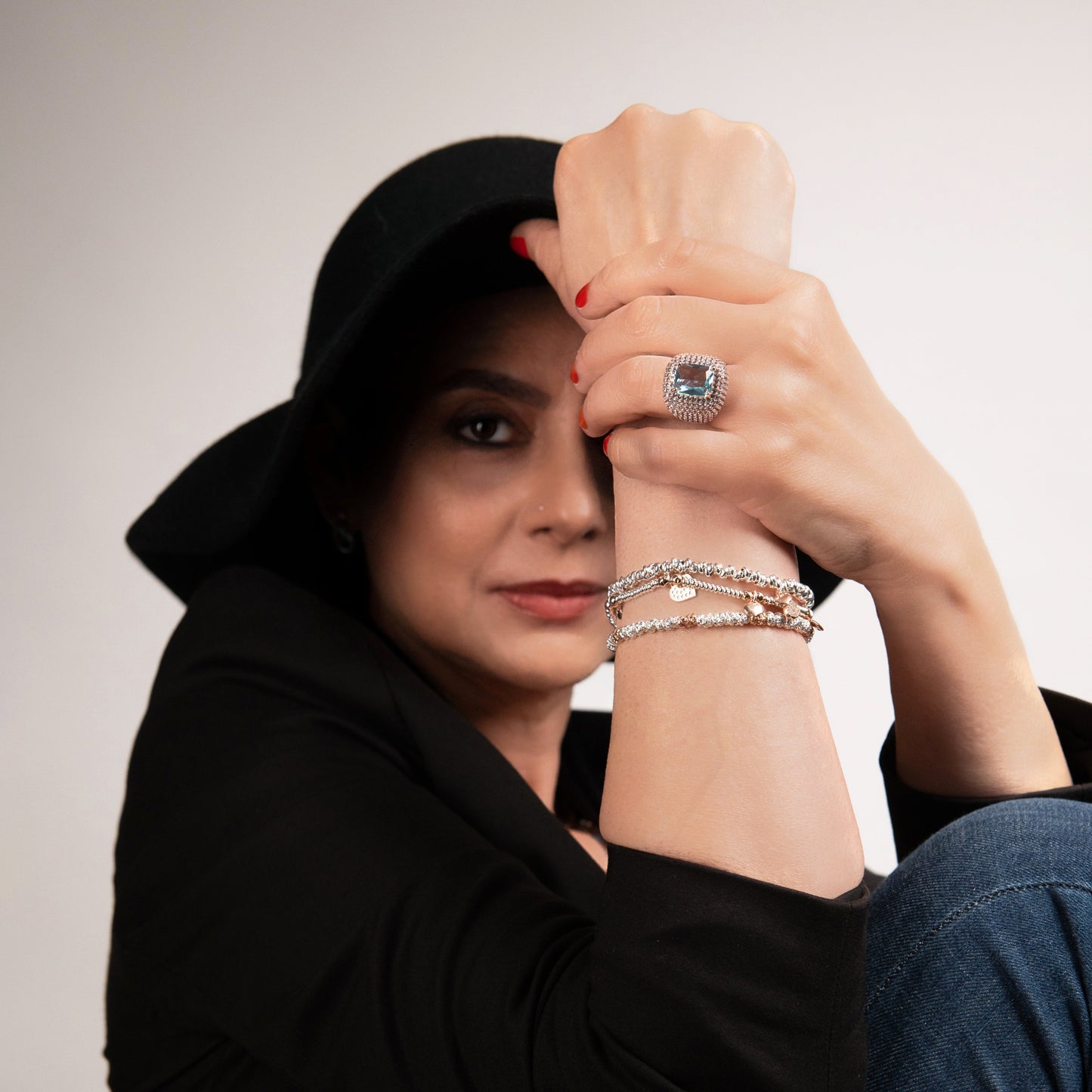Donna elegante con cappello e anello grande, bracciali e unghie rosse, sguardo intenso.