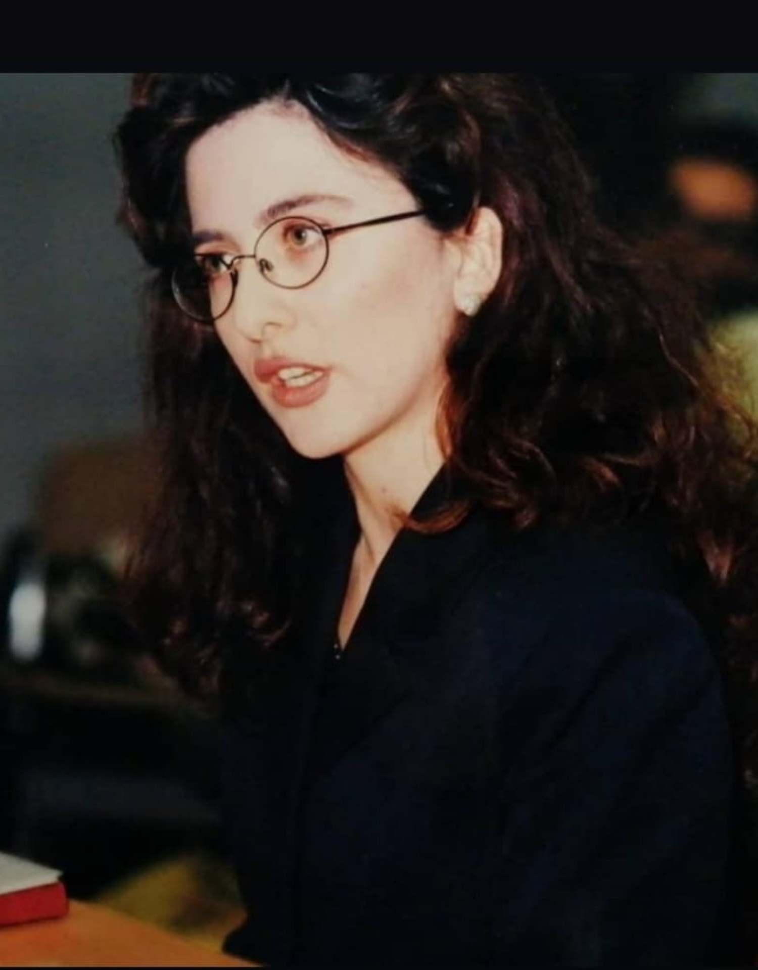 Donna con capelli castani e occhiali rotondi, indossa una giacca scura.