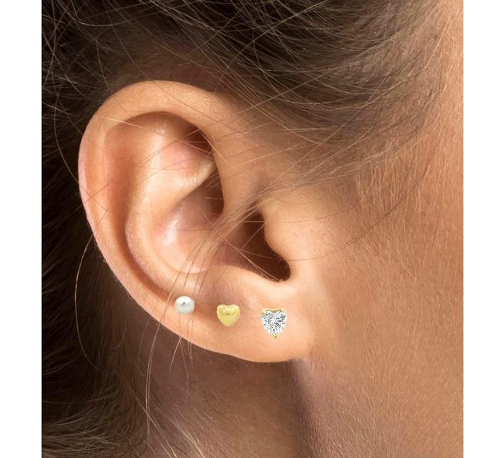 Un orecchio con tre orecchini: una perla, un cuore d'oro e un cuore di diamante.