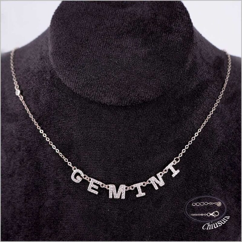 Collana d'argento con la parola "GEMINI" tempestata di gemme, esposta su un manichino nero.